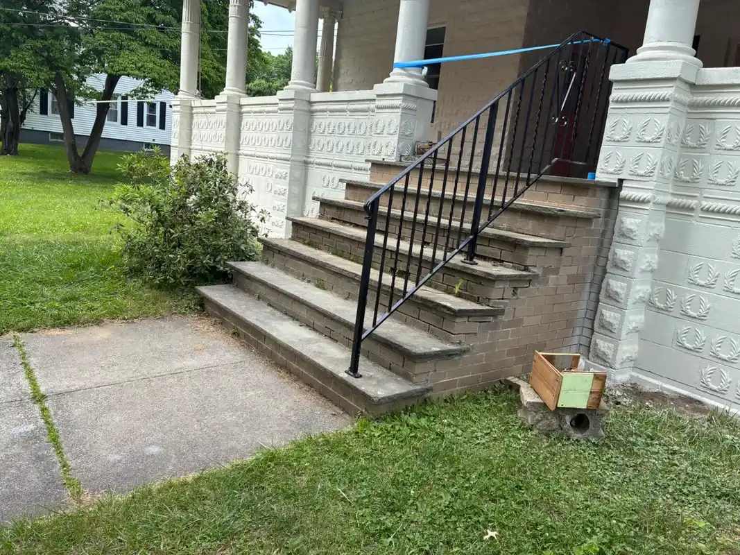 Brick steps with a black metal railing and white stone pillars.