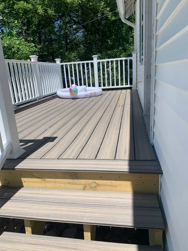 New composite wood deck with white railings and stairs on a house.