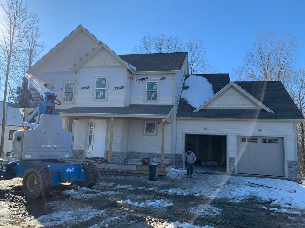 Construction site of a house with siding and a blue boom lift.