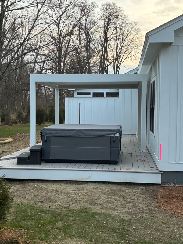 Grey hot tub on a wooden deck under a white pergola.