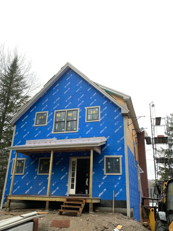 House under construction with blue weather barrier wrap and wooden framing.