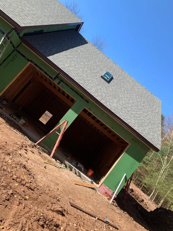 House under construction with green house wrap and grey shingled roof.