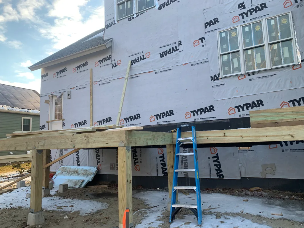 House under construction with new wooden deck framing and Typar house wrap.