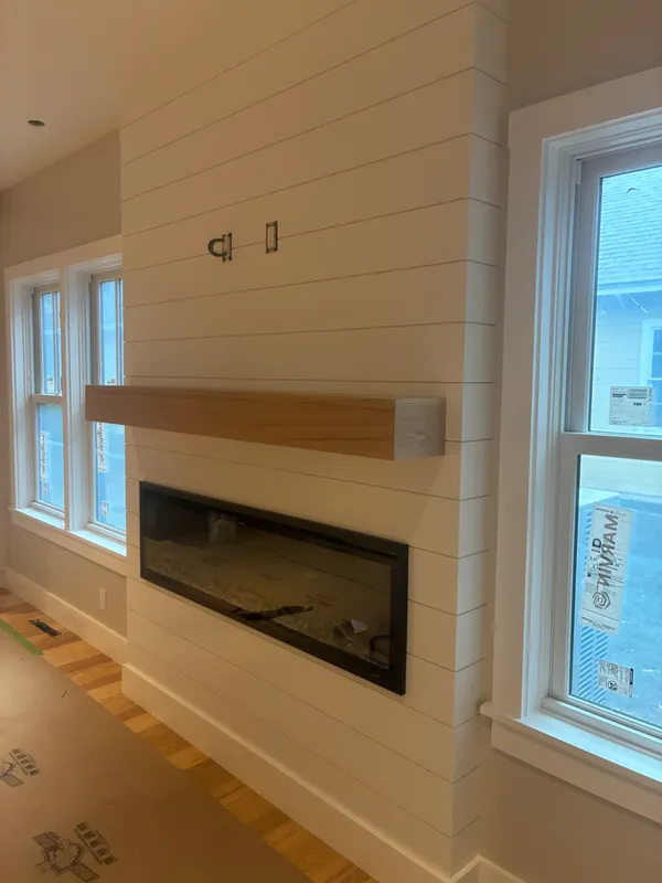 Modern living room with white shiplap wall, fireplace, and wood mantel.