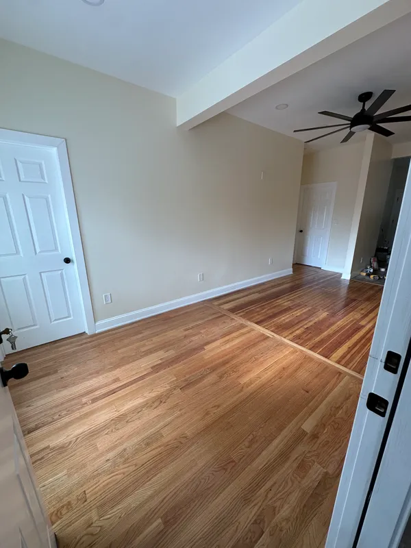 Newly installed hardwood flooring in a spacious room with white walls.