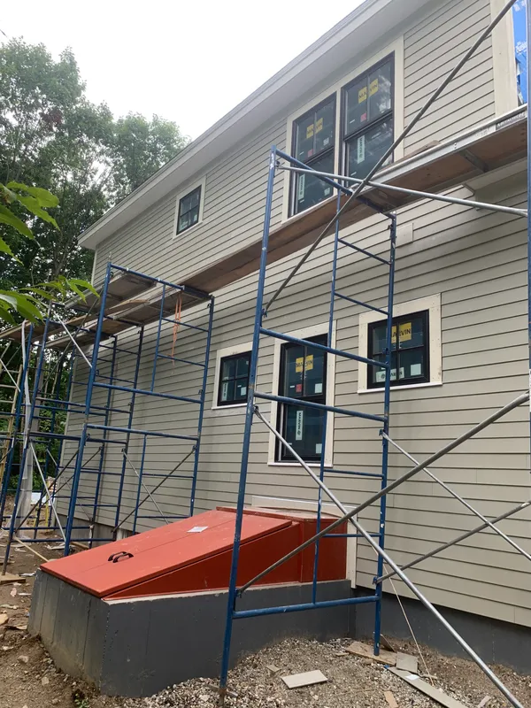 Scaffolding set up against a house with gray siding and new windows.