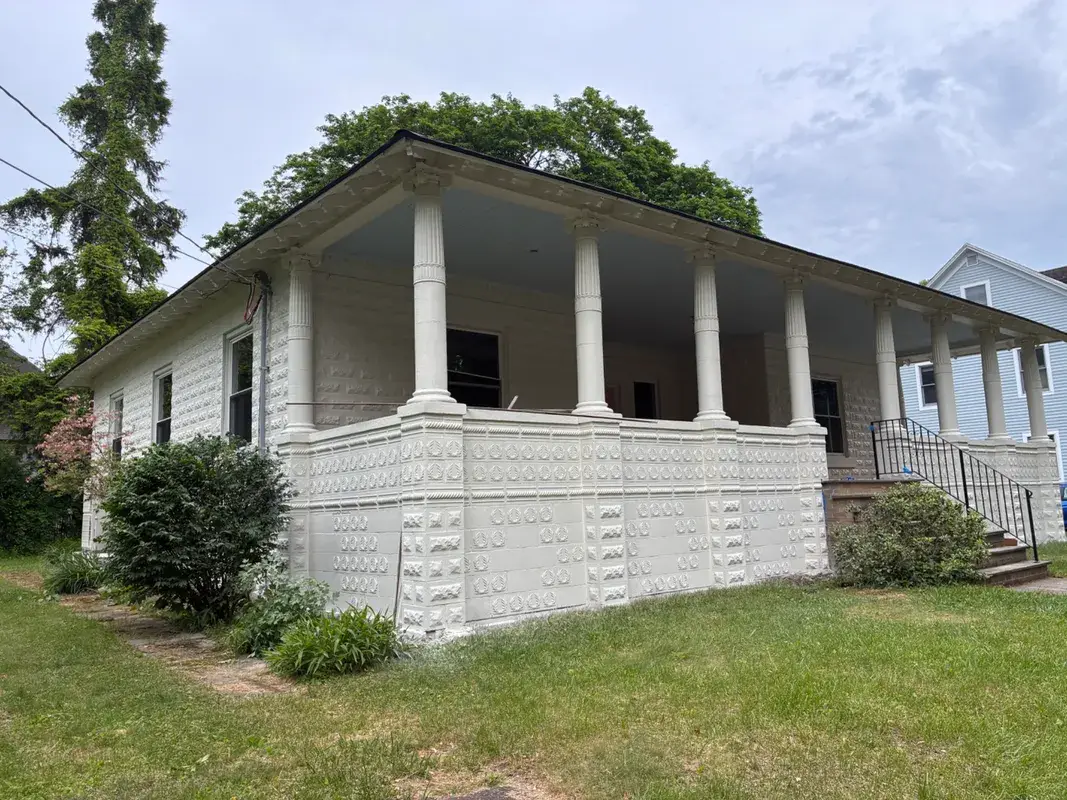 White house with a large covered porch and decorative stone pillars.