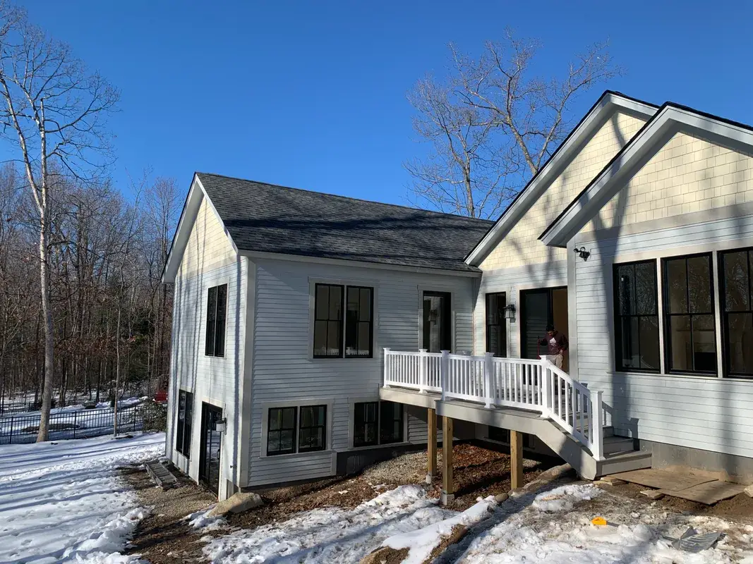 White siding house with a new deck and black windows in snow.