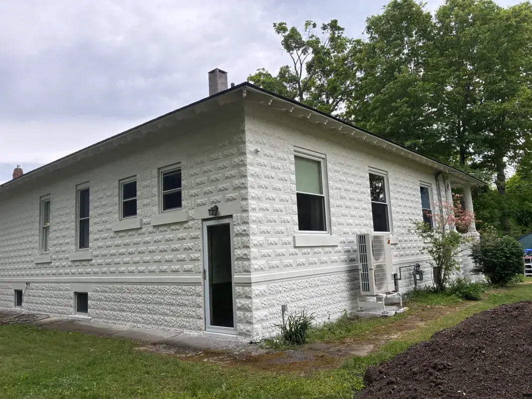 White textured stone house with a dark roof and green lawn.