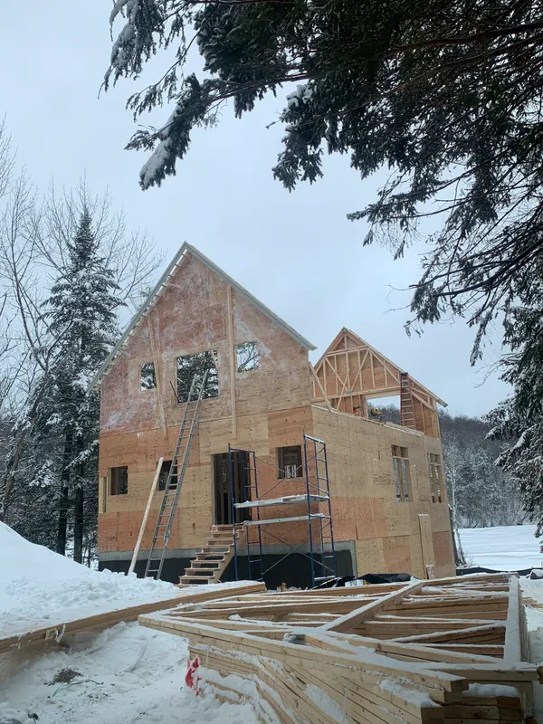 Wood frame house under construction in a snowy winter landscape.