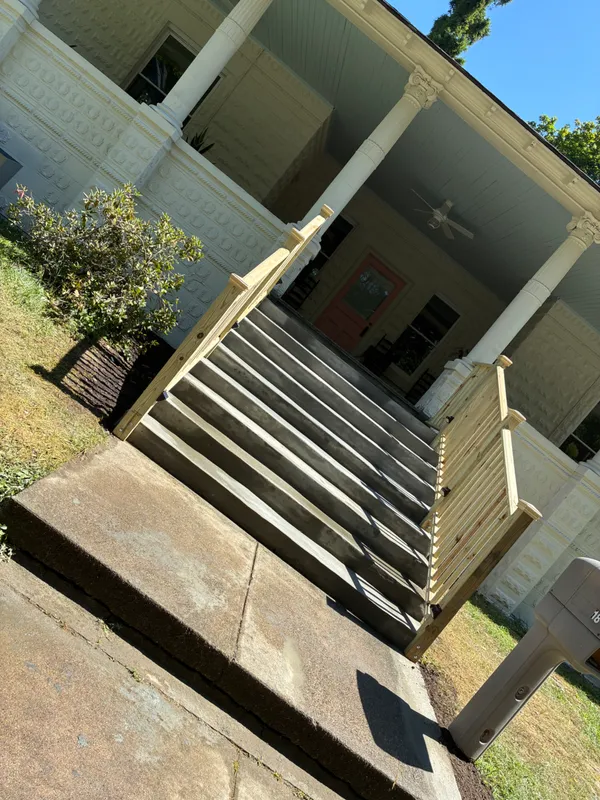 Wooden stairs and railing leading to a porch of a house.