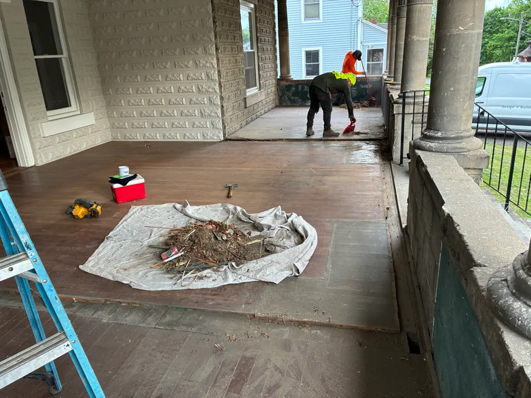 Workers power washing a wooden porch and deck of a house.